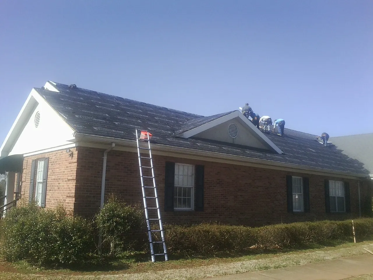 Crew tearing shingles off a brick ranch roof with a ladder set — Metal Roof Repair work by our crew in Lakeview