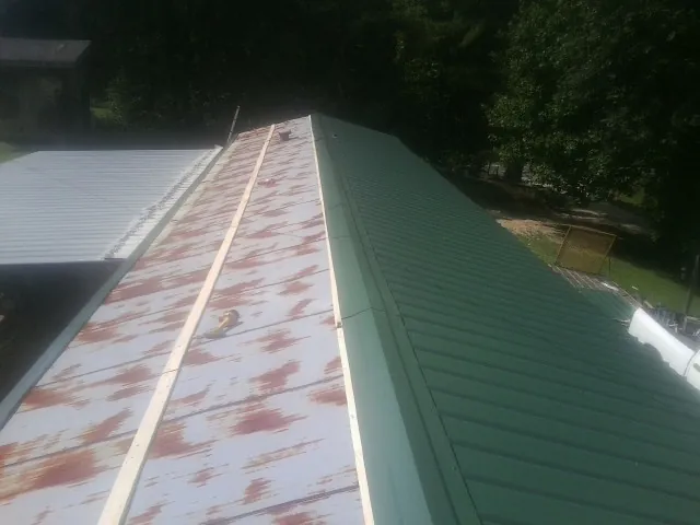 Old rusted panels beside newly installed green metal roofing — Wind Damage Roof Repair by Roofing Brothers in Lakeview
