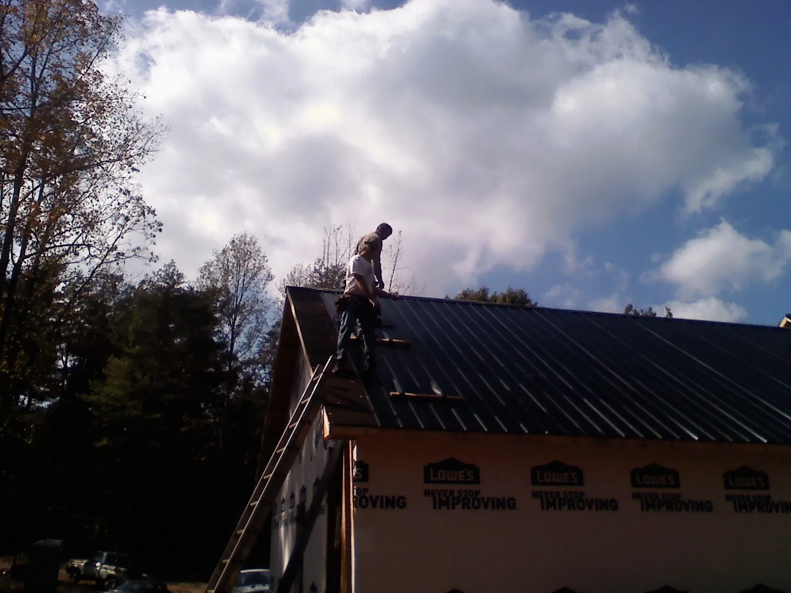 Roofer fastening dark metal panels high against a cloudy sky, from a Roof Inspection job in Lakeview