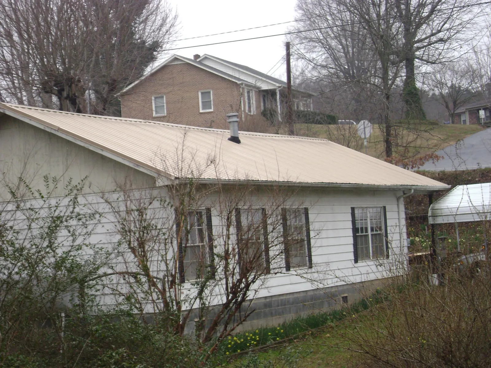 Tan metal roof on a white sided house set into a hillside — Commercial Roofing by Roofing Brothers in Lakeview